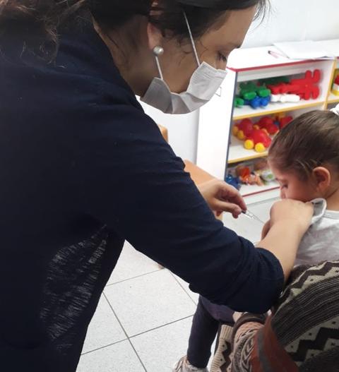 Una profesional de la salud está administrando una vacuna a una niña en un consultorio médico.