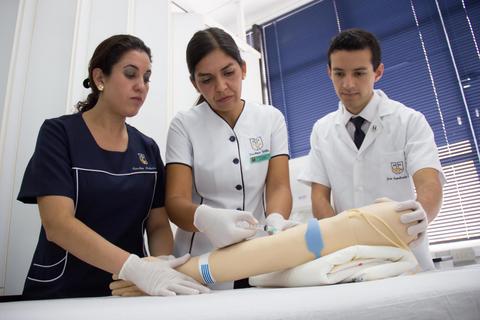 Tres profesionales de la salud realizan una práctica de inyección en un brazo simulado.