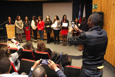 Un grupo de personas participa en una ceremonia de entrega de diplomas mientras algunos asistentes toman fotos.