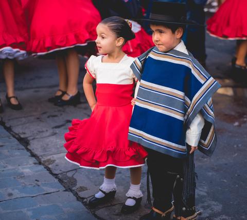 Dos niños vestindo trajes tradicionales, uno en una vestimenta roja y una niña con un vestido blanco y rojo.