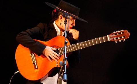 Una mujer toca una guitarra mientras viste un atuendo tradicional con sombrero.