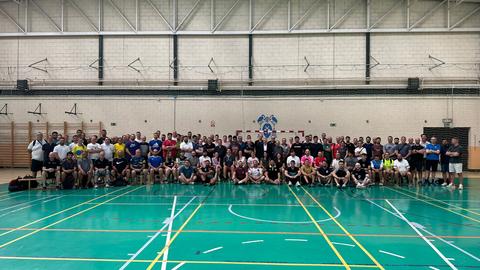 Un gran grupo de personas posando en un gimnasio, todas vestidas con camisetas y shorts deportivos.