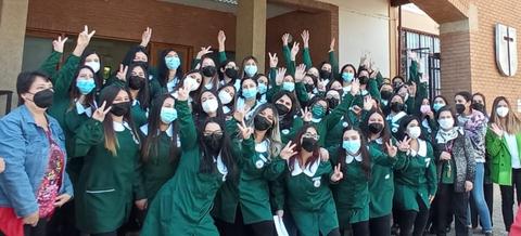 Un grupo de estudiantes en uniforme posando con gestos de alegría frente a un edificio.