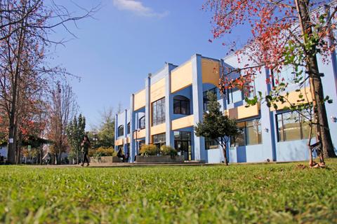 Edificio moderno con fachadas azules y amarillas, rodeado de árboles y césped.