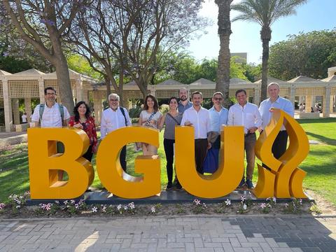 Un grupo de personas posando frente a un gran letrero que dice BGU en un entorno al aire libre.