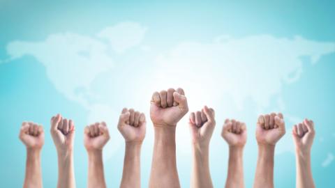 Un grupo de puños levantados en señal de unidad y protesta frente a un fondo de mapa mundial.