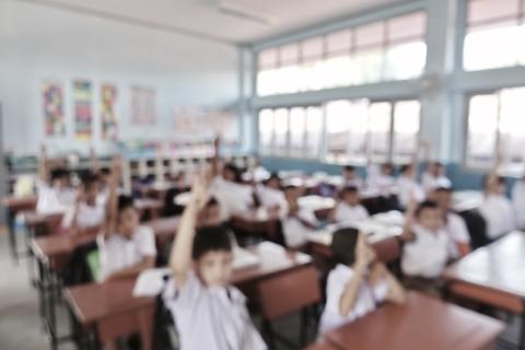 Una clase de estudiantes levantando la mano en un aula.