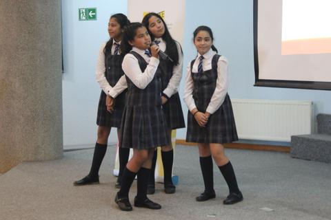Cuatro estudiantes en uniforme presentan un proyecto en un escenario.