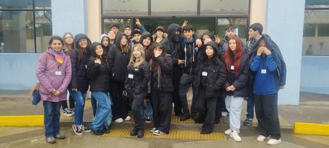 Un grupo de jóvenes posando juntos en la entrada de un edificio escolar.