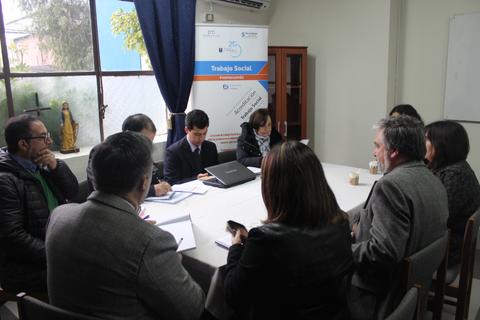 Una reunión de varios profesionales discutiendo en torno a una mesa con documentos y computadoras portátiles.