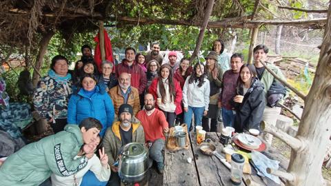 Un grupo grande de personas sonríe y posa juntos al aire libre, bajo una estructura rústica.
