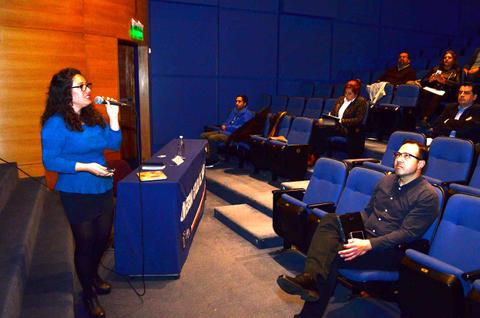 Una mujer presenta en un auditorio mientras el público la observa atentamente.