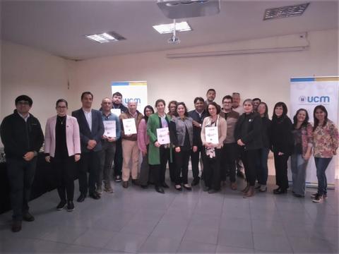 Un grupo de personas posan juntas en un evento en un aula con carteles de UCM.