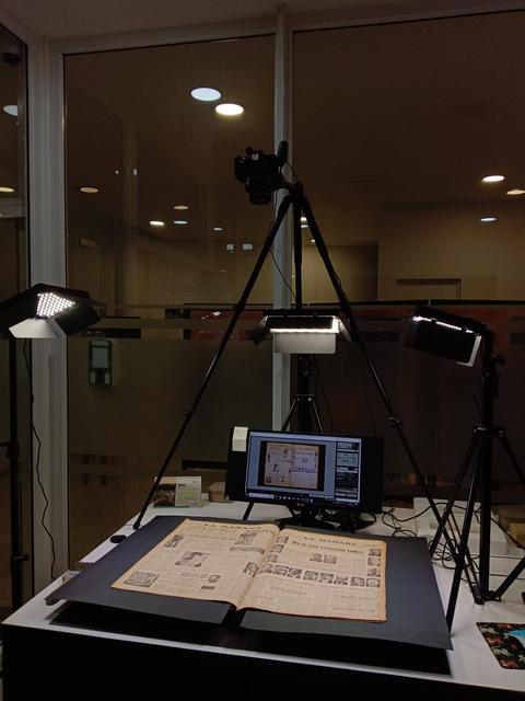 La imagen muestra un dispositivo de digitalización de documentos con un libro abierto y varias luces de estudio.