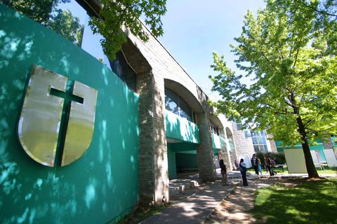 Un edificio de arquitectura moderna rodeado de árboles y personas caminando.