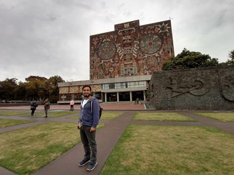 Un hombre posa frente a un edificio con murales y jardines en un día nublado.