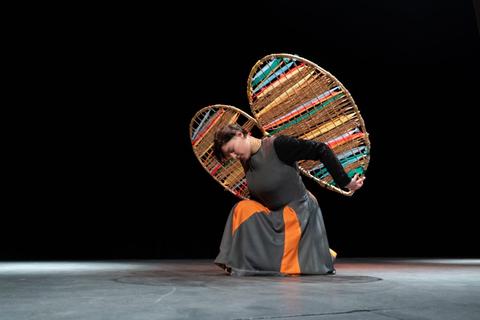 Una mujer baila con grandes sombreros decorativos en un escenario oscuro.