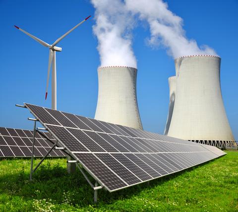 La imagen muestra paneles solares, un aerogenerador y torres de enfriamiento de una planta nuclear bajo un cielo azul.