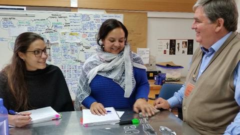 Un grupo de personas sonrientes se reúne alrededor de una mesa llena de documentos y materiales de trabajo.