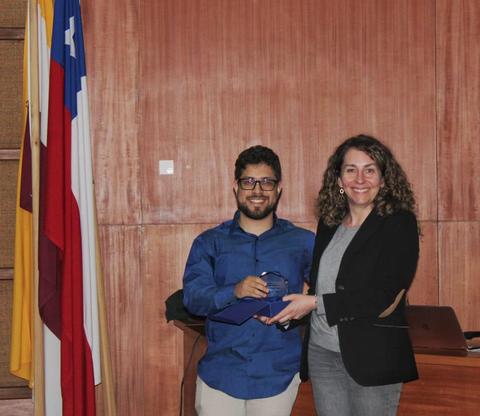 Un hombre y una mujer se están entregando un objeto en un acto formal frente a banderas.