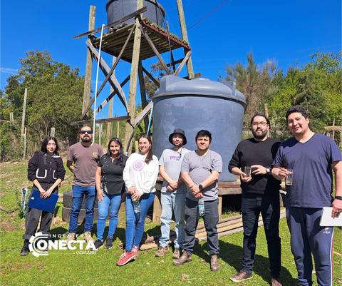 Un grupo de personas posando frente a un tanque de agua en un entorno natural.