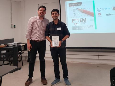 Dos hombres posan juntos sonrientes después de un evento, uno sosteniendo un premio o reconocimiento.