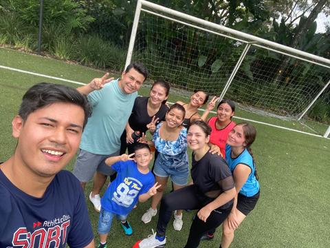 Un grupo de amigos sonríen y hacen señales de paz en un campo de fútbol.