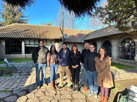 Un grupo de siete personas posa frente a un edificio en un entorno natural con cielo despejado.
