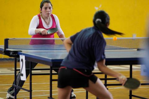 Dos jugadoras compiten en una partida de tenis de mesa en un gimnasio.