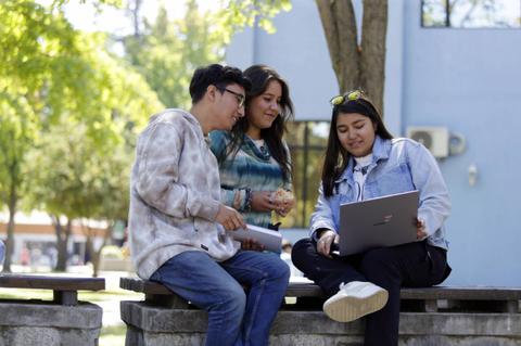 Tres estudiantes se reúnen al aire libre para trabajar en un proyecto con una laptop.