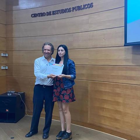 Una mujer y un hombre sostienen un documento en un evento de entrega de certificados.
