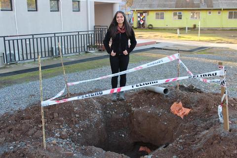 Una joven posa junto a un agujero en el suelo que está marcado con cinta de advertencia.