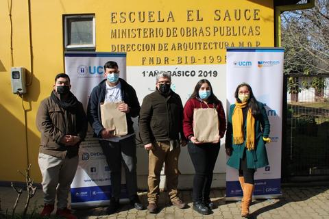 Un grupo de personas posa sonriente frente a un edificio con un cartel que indica la Escuela El Sauce.