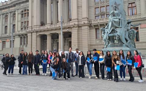 Un grupo de estudiantes posando frente a un edificio histórico con una estatua en el centro.