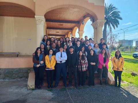 Un grupo grande de personas posando juntas en un lugar al aire libre, con un fondo de edificios y palmeras.
