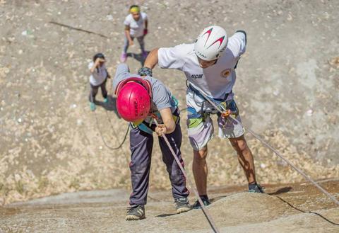 Un instructor ayuda a un escalador a ascender una pared de roca mientras otros escaladores observan.