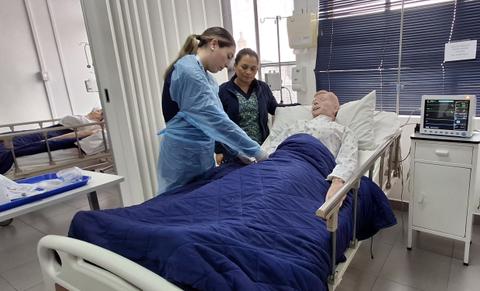 Dos mujeres están atendiendo a un paciente simulado en una habitación de hospital.