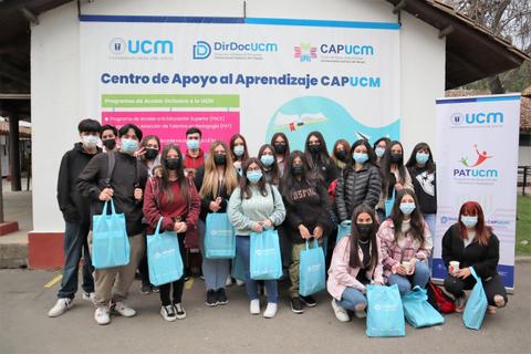Un grupo de estudiantes posa frente a un centro de apoyo al aprendizaje, todos usando mascarillas y sosteniendo bolsas azules.