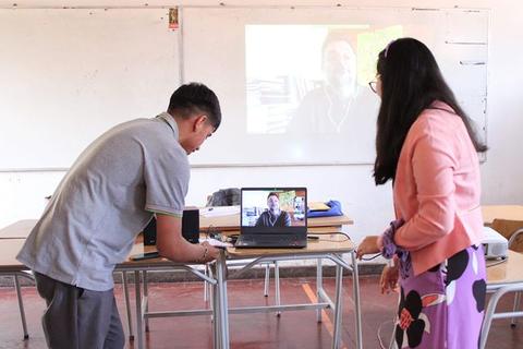 Un hombre y una mujer en un aula, interactuando con un ordenador portátil que muestra a un conferencista en línea.