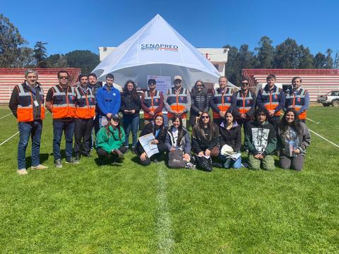 Un grupo de personas posando frente a una carpa de SENAPRED en un campo deportivo.