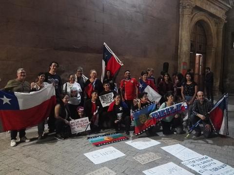 Un grupo de personas se reúne en un espacio público en Chile, sosteniendo banderas y carteles.