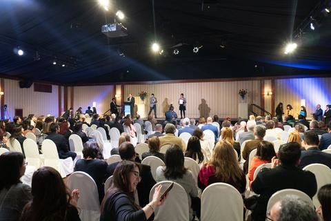 Una multitud de personas sentadas en un evento con un escenario al fondo.