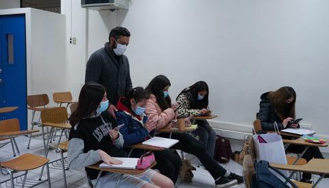 Un grupo de estudiantes se encuentra en un aula usando mascarillas y utilizando sus teléfonos móviles.