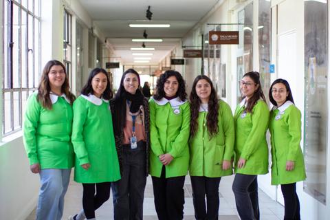 Grupo de mujeres sonrientes vestidas con chaquetas verdes en un pasillo.