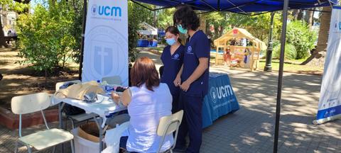 Una feria de salud en un parque con personal médico atendiendo a una persona en una mesa.