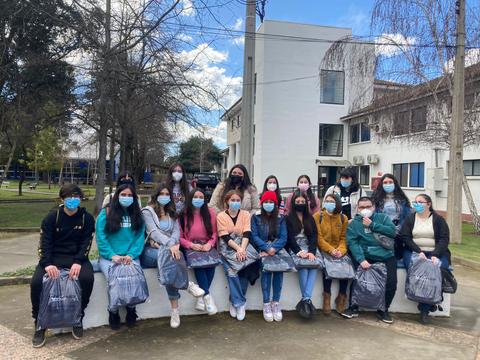 Grupo de estudiantes posando al aire libre, todos con mascarillas y sosteniendo bolsas.