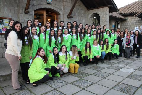 Un grupo de mujeres sonrientes vestidas con chaquetas verdes posa en una foto grupal frente a un edificio de piedra.