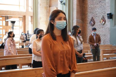 Un grupo de personas con mascarillas observa en un recinto con bancos de madera.