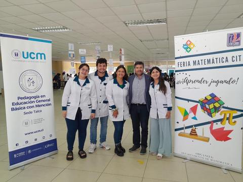 Grupo de estudiantes y un profesor participan en la Feria Matemática en un ambiente educativo.