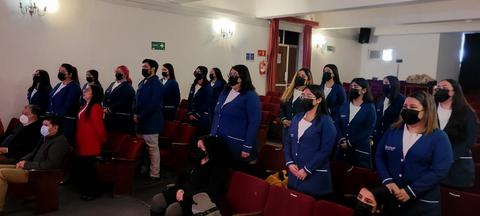 Un grupo de personas vestidas con chaquetas azules y mascarillas, de pie en un auditorio.
